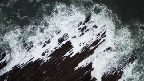 Birdseye-Luftaufnahme-Von-Meereswellen,-Die-An-Einem-Kalten-Herbsttag-In-Irland-Auf-Die-Zerklüftete-Felsige-Küste-Schlagen,-Drohnenaufnahme-Von-Oben-Nach-Unten