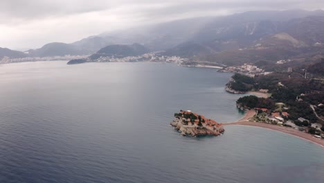 AERIAL---Sveti-Stefan-island,-tombolo,-and-Villa-Milocer-in-Montenegro,-backwards