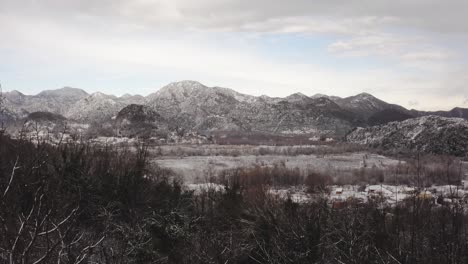 AERIAL---Forest-and-mountains-around-village-of-Virpazar-in-snowy-winter,-Montenegro