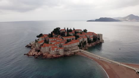 AERIAL---Sveti-Stefan-island-and-its-tombolo,-Adriatic-Sea,-Montenegro,-spinning-shot