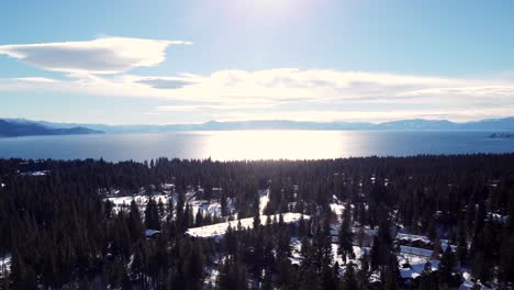 Aerial-drone-shot,-view-over-the-crystal-clear-lake-while-descending-in-the-woods-in-Lake-Tahoe,-Nevada-California