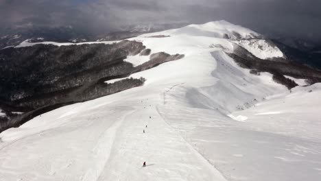AERIAL---People-skiing-in-mountains-at-Kolasin-ski-resort,-Montenegro,-forward-tilt-up