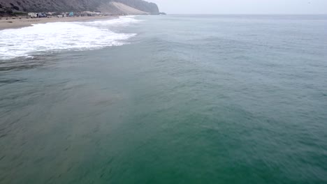 Aerial-drone-shot,-drone-flying-fast-over-the-ocean-and-ascending-in-Point-Mugu-State-Park,-Santa-Monica,-California