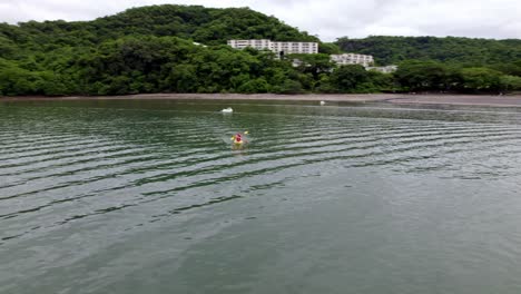 Aerial-orbit-over-two-people-doing-kayaking-in-sea-near-Planet-Hollywood-hotel-between-woods,-Nacascolo-beach,-Papagayo-Peninsula,-Costa-Rica