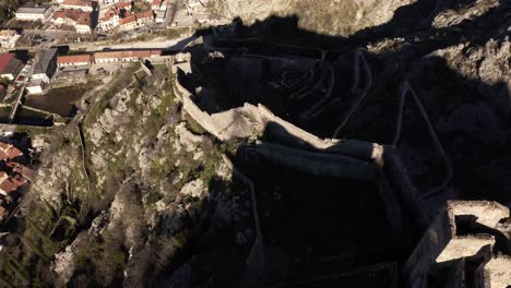 AERIAL---Ancient-city-walls-in-Kotor,-Montenegro,-forward-tilt-down-to-top-down