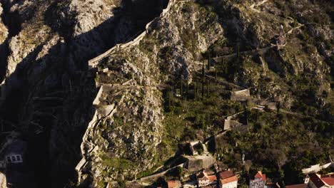 AERIAL---Ancient-city-walls,-Kotor,-Montenegro,-a-UNESCO-World-Heritage-Site,-tilt-up
