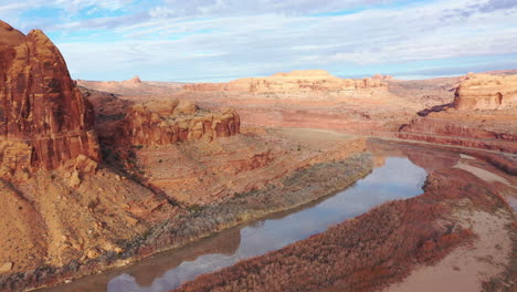 Red-rock-mountains-and-desert-with-river-flowing-through,-aerial-pan-right-view