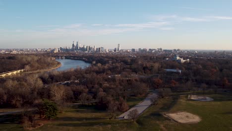Aerial-dolly-drone-shot,-drone-flying-over-some-treetops-moving-backward-from-the-Philadelphia-skyscraper-skyline,-Pennsylvania