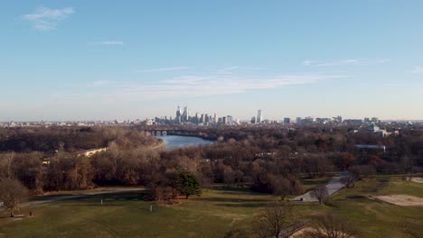 Aerial-drone-shot,-drone-flying-over-some-treetops-towards-the-Philadelphia-skyscraper-skyline,-Pennsylvania