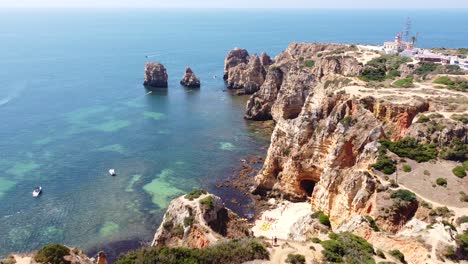 Ponta-Da-Piedade,-Lagos,-Algarve,-Portugal---Aerial-Drone-View-of-the-Coastline-with-Walking-Path,-Rocky-Cliffs,-Hidden-Beach,-Boat,-Kayaks-and-Clear-Sea