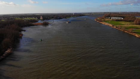 Aerial-Over-Oude-Maas-Rising-To-Reveal-Zwijndrecht-Landscape-With-Colorado-Cargo-Ship-In-Distance