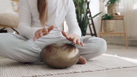 Woman-playing-a-handpan-in-her-living-room,-female-musician-using-a-relaxing-zen-musical-instrument