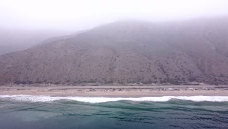 Aerial-drone-shot,-drone-flying-over-the-ocean-towards-the-coastline-and-mountains-in-Point-Mugu-State-Park,-Santa-Monica,-California