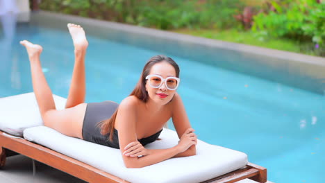 Eine-Junge-Attraktive-Frau-In-Einem-Badeanzug-Mit-Sonnenbrille-Liegt-Auf-Einer-Sonnenliege-Neben-Einem-Schwimmbad