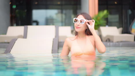 Eine-Junge-Attraktive-Frau,-Die-Sich-In-Einem-Schwimmbad-Entspannt,-Hebt-Ihre-Hand,-Um-Ihre-Sonnenbrille-Anzupassen