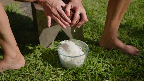 Slow-motion-close-up-of-woman-shredding-fresh-coconut-into-bowl-using-hand-scraper