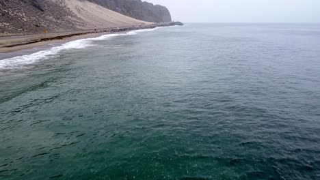 Aerial-drone-shot,-drone-flying-over-the-ocean-along-the-highway-in-Point-Mugu-State-Park,-Santa-Monica,-California