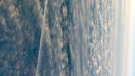 Uncommon-view-from-cockpit-of-flying-airplane-above-clouds-leaving-long-white-condensation-vapor-air-trail-in-blue-sky