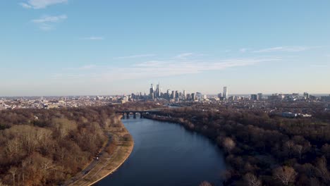 Aerial-drone-shot,-drone-flying-over-a-river-moving-towards-the-Philadelphia-skyscraper-skyline,-Pennsylvania