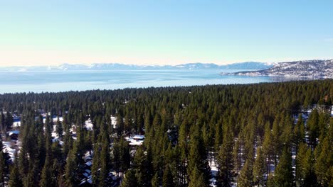 A-stunning-aerial-drone-shot,-flying-over-the-woods-towards-the-crystal-clear-lake-in-Lake-Tahoe,-Nevada-California