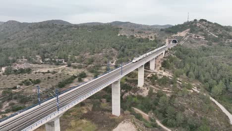 A-bullet-train-is-exiting-a-tunnel-and-moving-along-the-concrete-bridge-in-the-middle-of-a-beautiful-landscape-in-rural-Spain