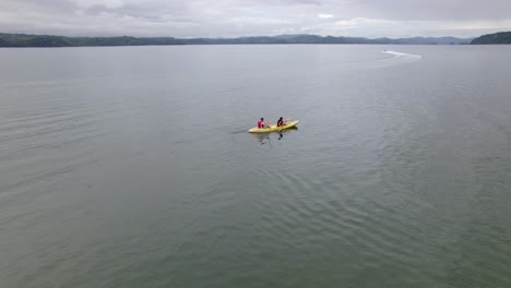 Aerial-orbit-of-people-doing-kayaking-in-calm-sea-near-dock-and-hills-covered-in-woods,-Nacascolo-beach,-Papagayo-Peninsula,-Costa-Rica
