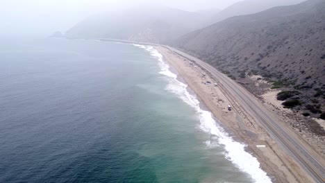 Aerial-drone-shot,-drone-flying-high-over-the-ocean-along-the-highway-in-Point-Mugu-State-Park,-Santa-Monica,-California