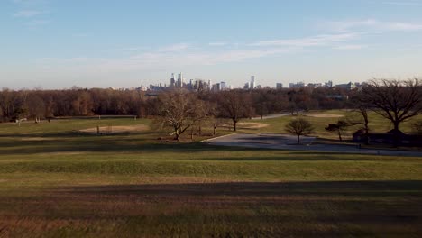 A-beautiful-aerial-drone-shot,-drone-flying-low-over-a-park-towards-the-Philadelphia-skyscraper-skyline,-Pennsylvania