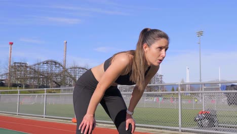 Young-athletic-woman-running-along-track-fatigued-stops-to-catch-breath