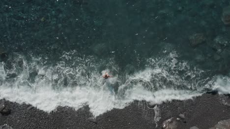 Top-down-of-woman-walking-into-clear-ocean-water-for-swimming-at-Madeira-shore,-summer-vacation