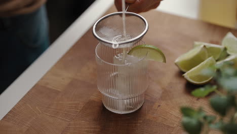 Young-Male-pours-a-cocktail-from-a-metal-mixer-through-a-sieve-into-a-modern-drinking-glass