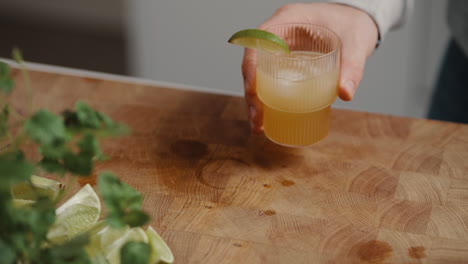 Young-male-grabbing-a-cocktail-in-a-modern-drinking-glass-from-a-wooden-cutting-board-the-kitchen-at-home