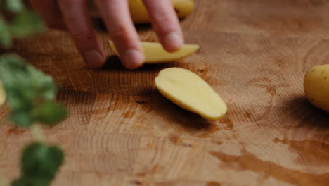 Male-chef-sliceing-potato-in-the-kitchen-on-a-wooden-cutting-board-in-the-kitchen
