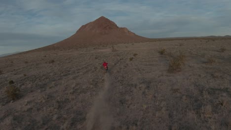 A-motorcyclist-speeds-through-the-Mojave-Desert's-rugged-terrain-at-sunset---aerial-follow-view