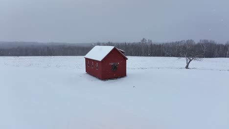 Little-red-cabin-sits-against-a-forest-backdrop-light-dusting-of-snow