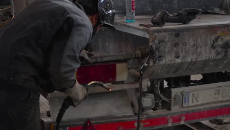 Worker-inspects-and-welds-dirty-truck-in-workshop