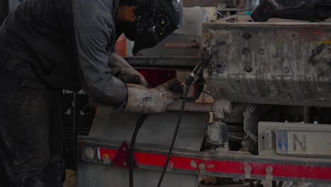 Worker-with-headpiece-welds-dirty-truck-in-workshop