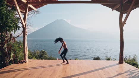 Attractive-slim-woman-doing-modern-dance-moves-on-wooden-floor-with-majestic-landscape-behind