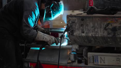 Worker-with-protective-gear-welds-dirty-truck-in-workshop