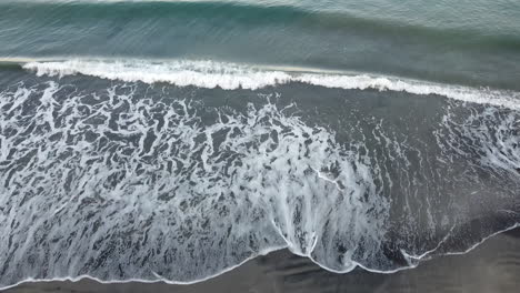 Drone-shot-of-waves-in-the-seashore-with-woman-walking