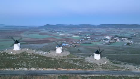 Drone-shot-of-the-view-of-the-famous-windmills-of-the-town-of-Consuegra,-symbol-of-Castilla-La-Mancha,-on-a-background-of-blue-sky-at-sunrise