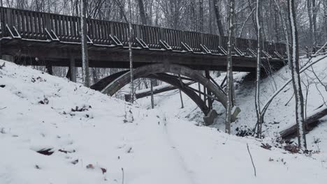Close-up-of-a-large-peaceful-arch-wooden-bridge-in-the-snow-over-a-frozen-creek-river-in-the-winter-during-the-snow