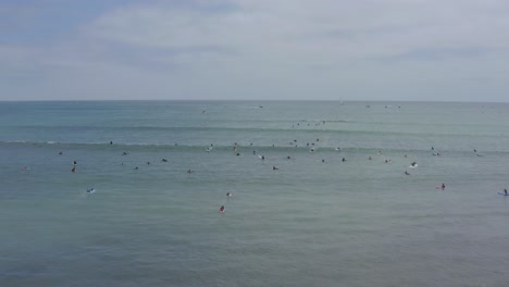 A-beautiful-aerial-drone-shot,-flying-backward-over-surfers-waiting-for-the-next-wave,-Dana-Point---Orange-County---California