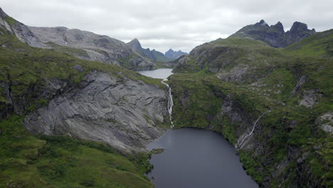 Aerial-dolly-forward-shot-of-dramatic-waterfall-in-the-mountains-with-rocky-cliffs-in-trolldalsvatnet,-lofoten,-Norway