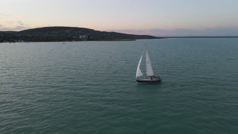 Aerial-arch-shot-circling-around-a-lone-sailboat-moving-along-Lake-Balaton,-Hungary