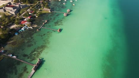 Upward-panning-drone-shot-of-the-lagoon-of-seven-colours-with-water-villas-and-sail-boats-in-the-horizon-located-in-Bacalar,-Mexico-in-4k