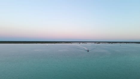 Wide-angle-establishing-drone-shot-of-a-beautiful-scene-of-the-lagoon-of-seven-colours-during-sunset-with-yachts-and-sail-boats-returning-to-the-pier-located-in-Bacalar,-Mexico-in-4k