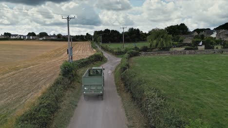 Rural-aerial-scene-with-a-tractor-driving-down-a-country-lane,-surrounded-by-fields-and-farmland