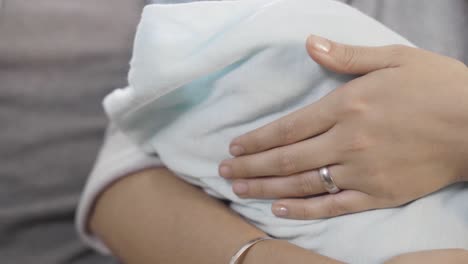 Close-up-shot-of-hands-of-a-young-mother-stroking-while-carrying-a-little-baby-wrapped-in-white-towel