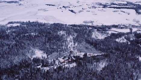 Far-away-aerial-drone-view-of-a-timber-logging-camp-in-the-middle-of-a-huge-snow-covered-valley-in-winter